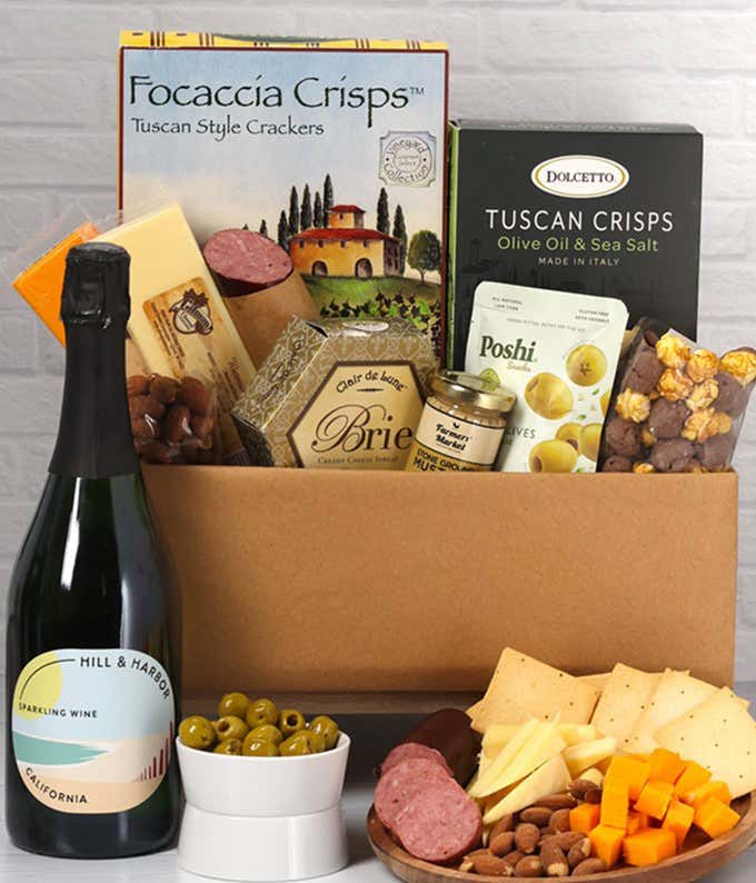 A charcuterie gift set with Tuscan crisps, focaccia crackers, 3 cheeses, olives, mustard, suasage almonds, chocolate-covered popcorn and a bottle of California Sparkling Wine.