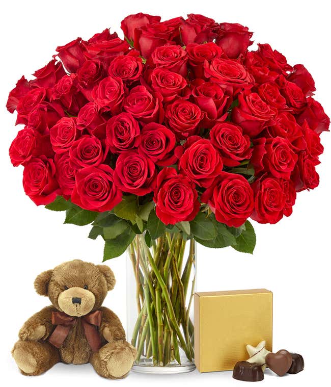 Image of 50 long-stemmed red roses in a tall cylinder vase, accompanied by a box of chocolates and a cuddly teddy bear, the perfect gift for expressing love and affection.