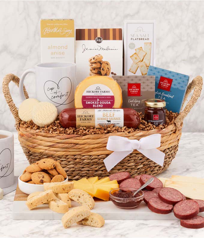 Sympathy gift basket in a woven tray with sausage, cheeses, flatbread, cookies, almond anise biscotti, tea, honey, two white mugs with “Cup of Comfort” design, and a white ribbon, displayed with a serving of meats, cheeses, cookies, and tea.