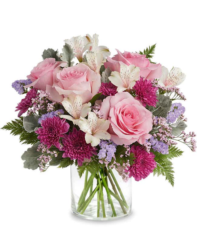 Image of a floral arrangement featuring Pink Roses, Ivory Alstroemeria, Purple Cushion Chrysanthemums, Lavender Sinuata Statice, Pink Limonium, and floral greens, presented in a keepsake Pink Shimmer Vase.