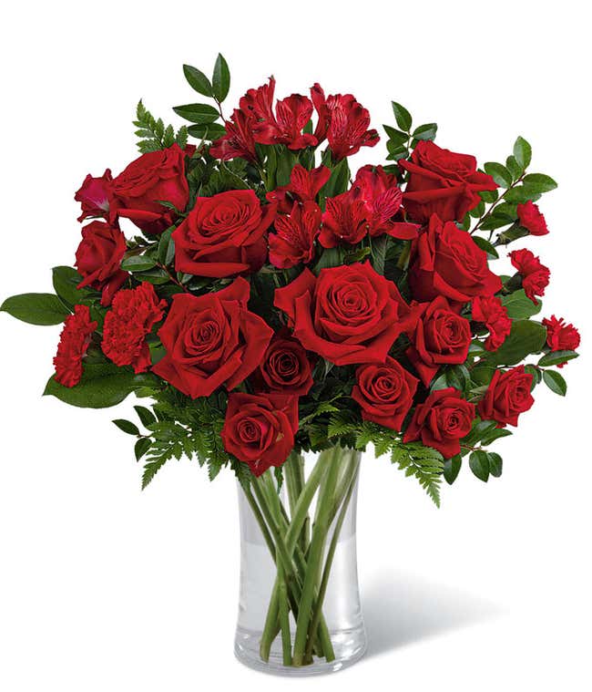 Red roses and red spray roses with floral greens in a tall clear cylinder glass vase