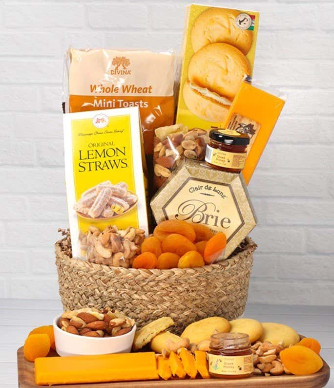 A two-toned woven basket filled with two cheeses, lemon flavored baked goods, crackers, dried apricots, gourmet nuts, and honey. 